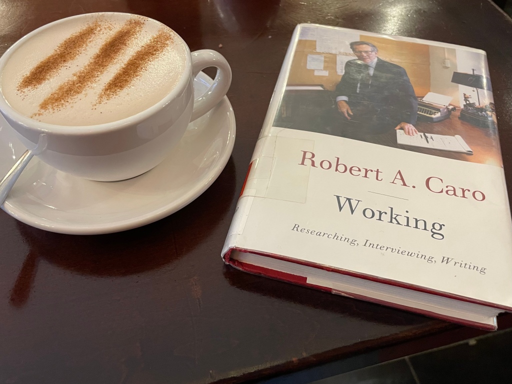 Copy of journalist and author Robert A. Caro's book, "Working: Researching, Interviewing, Writing," on a cafe table next to a chai latte in a white mug with cinnamon on top.