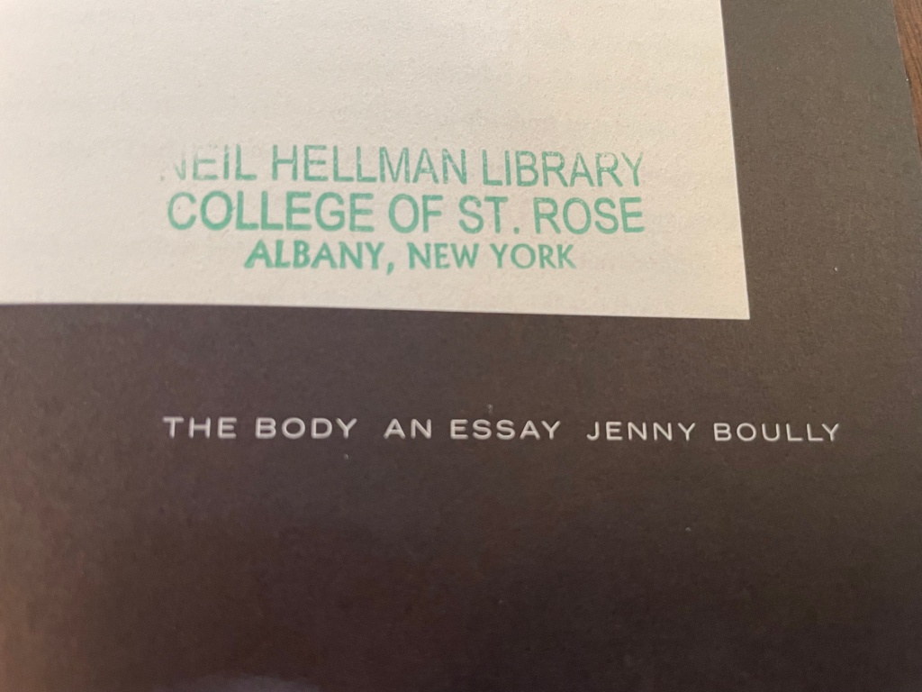 A corner of the title page of "The Body: An Essay" by Jenny Boully is stamped in green ink as belonging to the Neil Hellman Library at the College of St. Rose in Albany, New York.